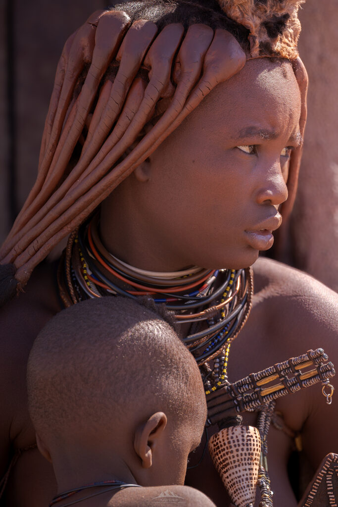 Madre Himba amamantando a su hijo en la región de Kunene, Namibia. Retrato documental con luz natural. Fotografía de Hugo Valle.